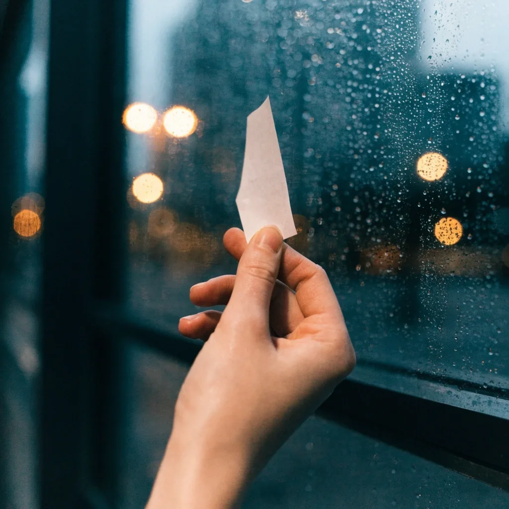 A paper receipt held between two fingers against a rain-streaked window